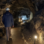 A traveler wearing a jacket and helmet inside a Mount Fuji lava cave