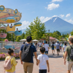 Families entering a colorful outdoor amusement park ride area near Mount Fuji