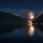 A distant fireworks display reflected across a mountain-enclosed lake at night
