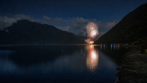 A distant fireworks display reflected across a mountain-enclosed lake at night