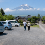 Travelers walking from a village parking area with Mount Fuji in the background