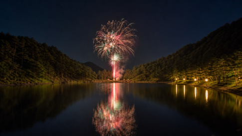 Fireworks reflecting across a quiet forested mountain lake at night