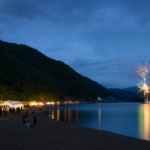 A small blue-hour lakeside festival with food stalls and brief fireworks over the water
