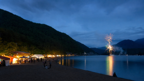 A small blue-hour lakeside festival with food stalls and brief fireworks over the water