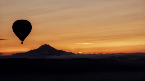 A hot-air balloon beside a mountain at sunrise