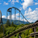 Three different steel roller coaster tracks in a mountain amusement park under a summer sky
