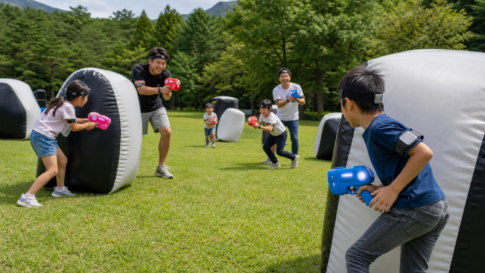 Text-free families playing a safe outdoor infrared tag game with colorful toy devices in a forest park
