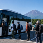 Hikers boarding an unbranded shuttle bus at a Fuji foothills parking area with Mount Fuji behind them
