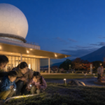 Text-free family using flashlights beside a geodesic radar dome at dusk with supervised sparklers in the plaza