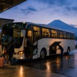 Travelers boarding an unbranded overnight coach at a Japanese terminal with a bare summer Mount Fuji beyond