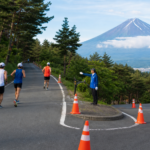 Runners and a course marshal on a traffic-controlled forest road below Mount Fuji