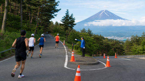 Runners and a course marshal on a traffic-controlled forest road below Mount Fuji