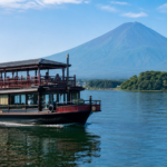 Unbranded traditional-style two-deck sightseeing boat cruising on Lake Kawaguchiko below snow-free Mount Fuji