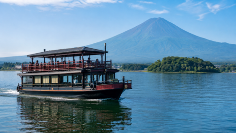 Unbranded traditional-style two-deck sightseeing boat cruising on Lake Kawaguchiko below snow-free Mount Fuji
