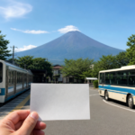 A blank travel pass held between a local train and route bus with snow-free Mount Fuji behind them
