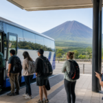 Text-free highway coach boarding hikers at a terminal with snow-free Mount Fuji behind