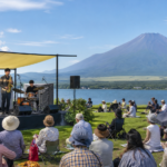 Text-free outdoor jazz ensemble performing for a lakeside audience with snow-free Mount Fuji