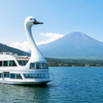 White swan-shaped sightseeing boat cruising on Lake Yamanaka with snow-free Mount Fuji beyond