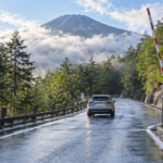 An open mountain toll road with a raised barrier and a car driving uphill after rain