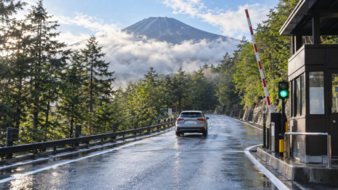An open mountain toll road with a raised barrier and a car driving uphill after rain