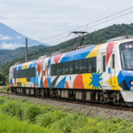 A colorful abstract-wrapped local train traveling through the foothills of Mount Fuji