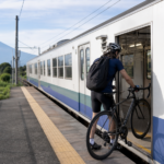 A cyclist rolling a road bicycle into a local train with Mount Fuji visible beyond the platform
