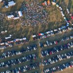 Aerial view of a busy outdoor concert area and its large temporary car park