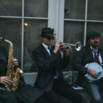 Three jazz musicians performing outdoors with saxophone, trumpet, and banjo