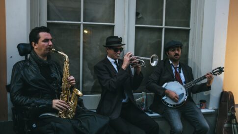 Three jazz musicians performing outdoors with saxophone, trumpet, and banjo