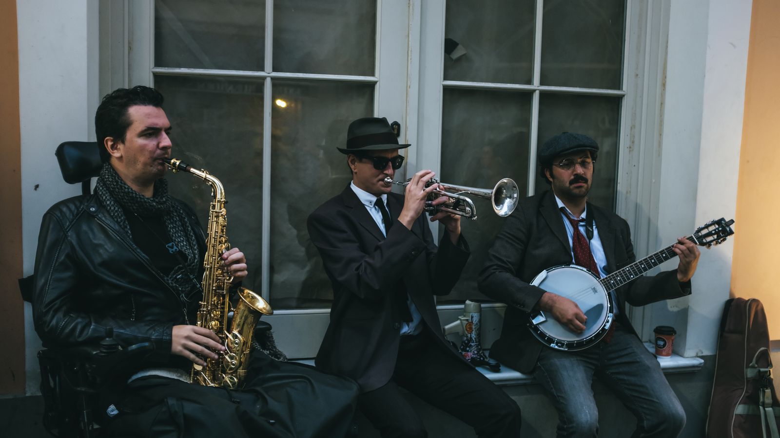 Three jazz musicians performing outdoors with saxophone, trumpet, and banjo