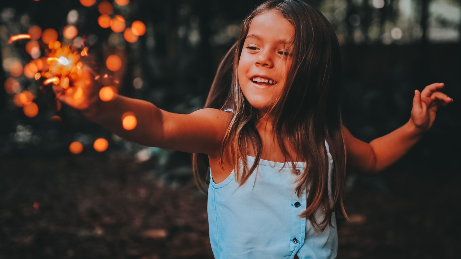 A child safely enjoying a handheld sparkler outdoors at dusk
