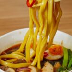 Thick Japanese noodles lifted from a spicy broth with a visible red chili pepper