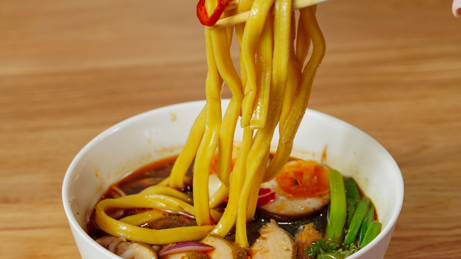 Thick Japanese noodles lifted from a spicy broth with a visible red chili pepper