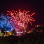 Fireworks illuminating the night sky above rides at an amusement park
