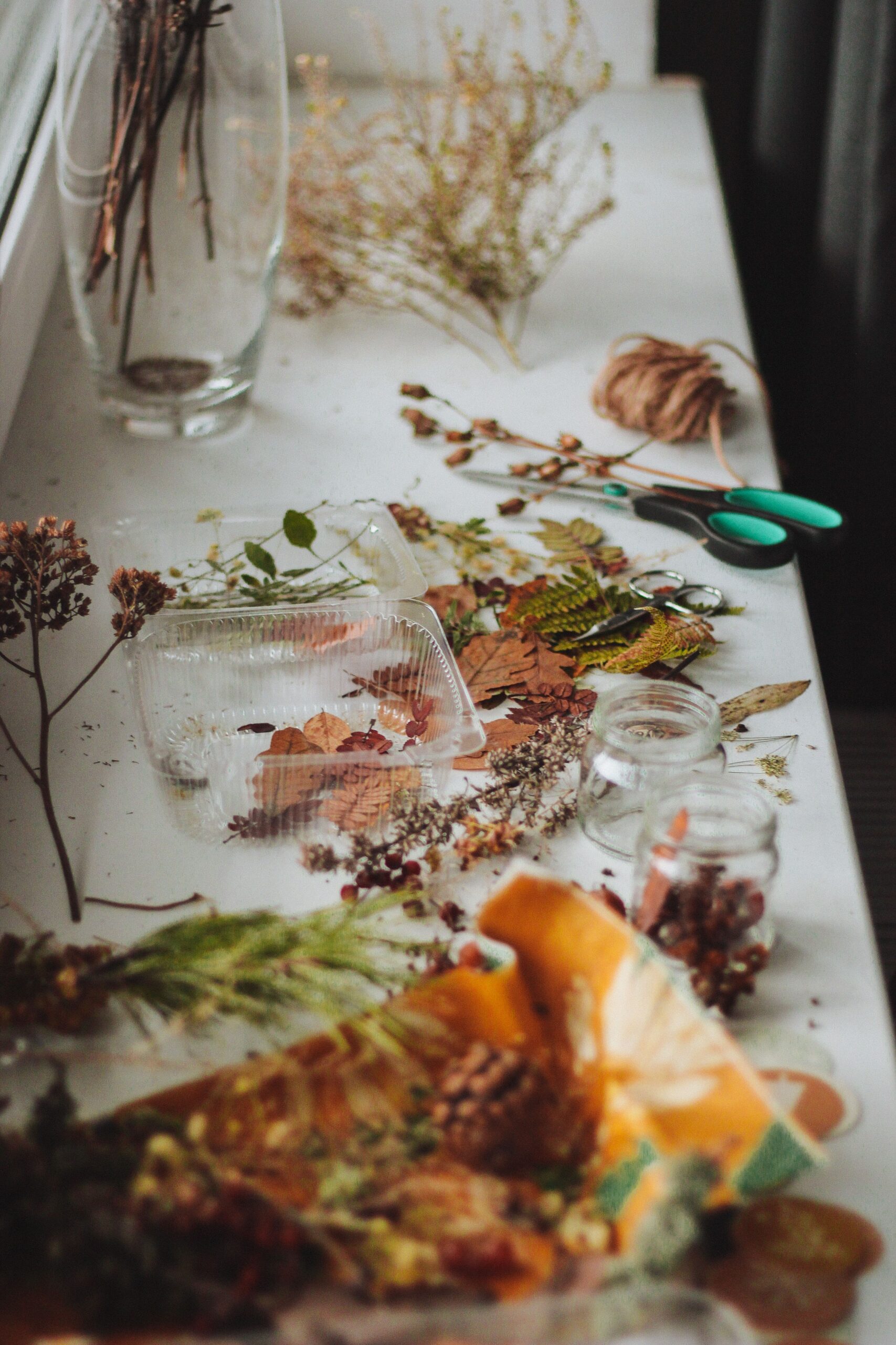 Dried flowers, twine, scissors and glass containers arranged for a botanical craft activity