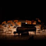 A grand piano and orchestra chairs waiting under stage lights in a concert hall