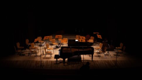 A grand piano and orchestra chairs waiting under stage lights in a concert hall