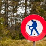 A red no-hiking symbol beside a forest trail