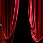 A microphone on a theater stage framed by red curtains