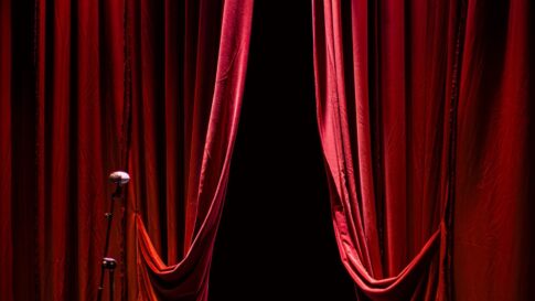 A microphone on a theater stage framed by red curtains