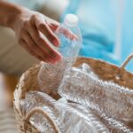 Hands sorting empty plastic bottles into a woven basket at home