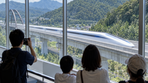 Visitors watching a high-speed maglev test train from an indoor observation gallery